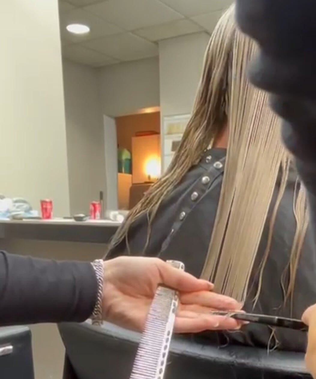 Lang blond haar wordt met kam en schaar op lengte geknipt.