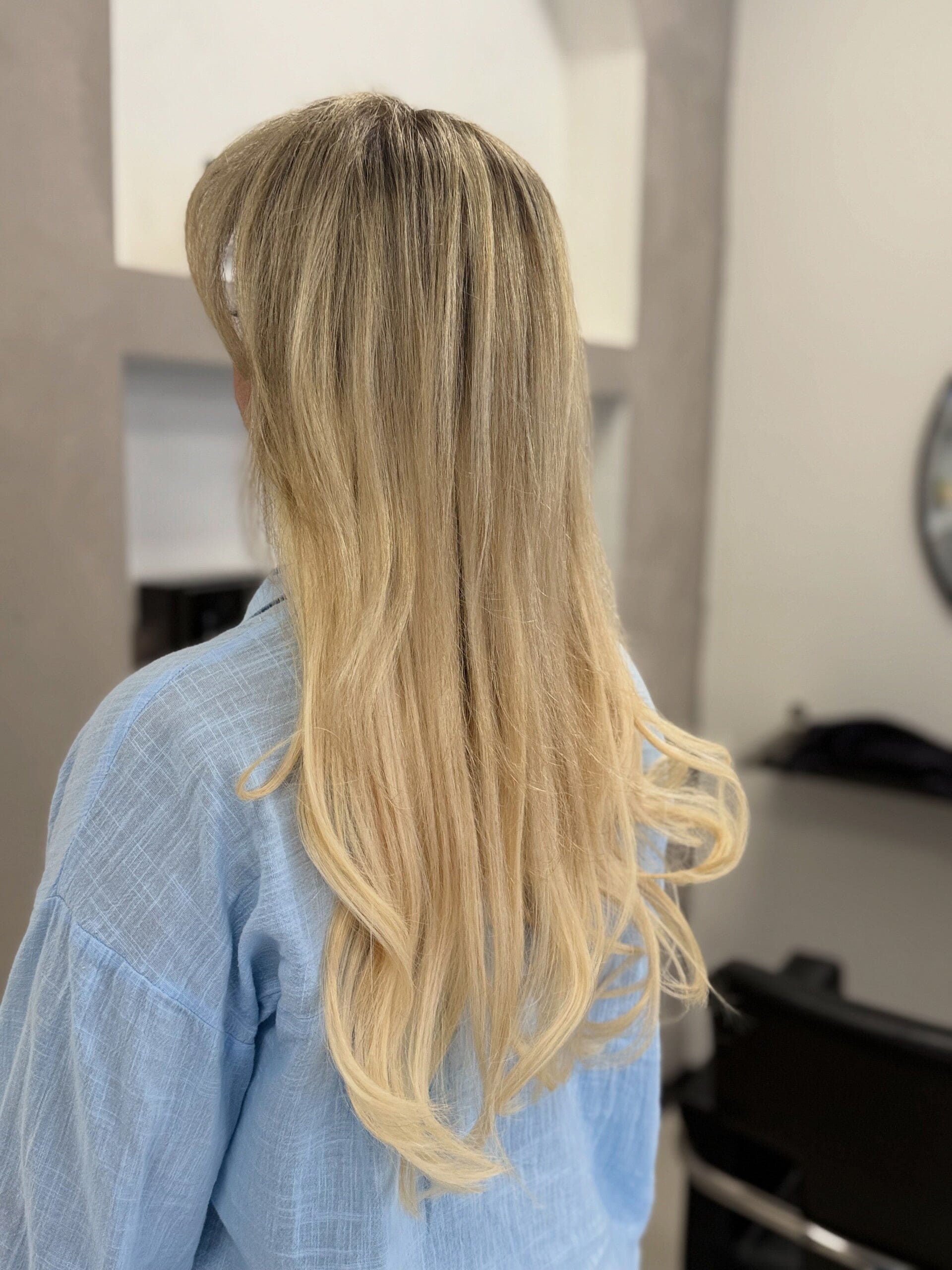 Lang blond haar met zachte krullen in de lengte, van achteren gezien in de salon.