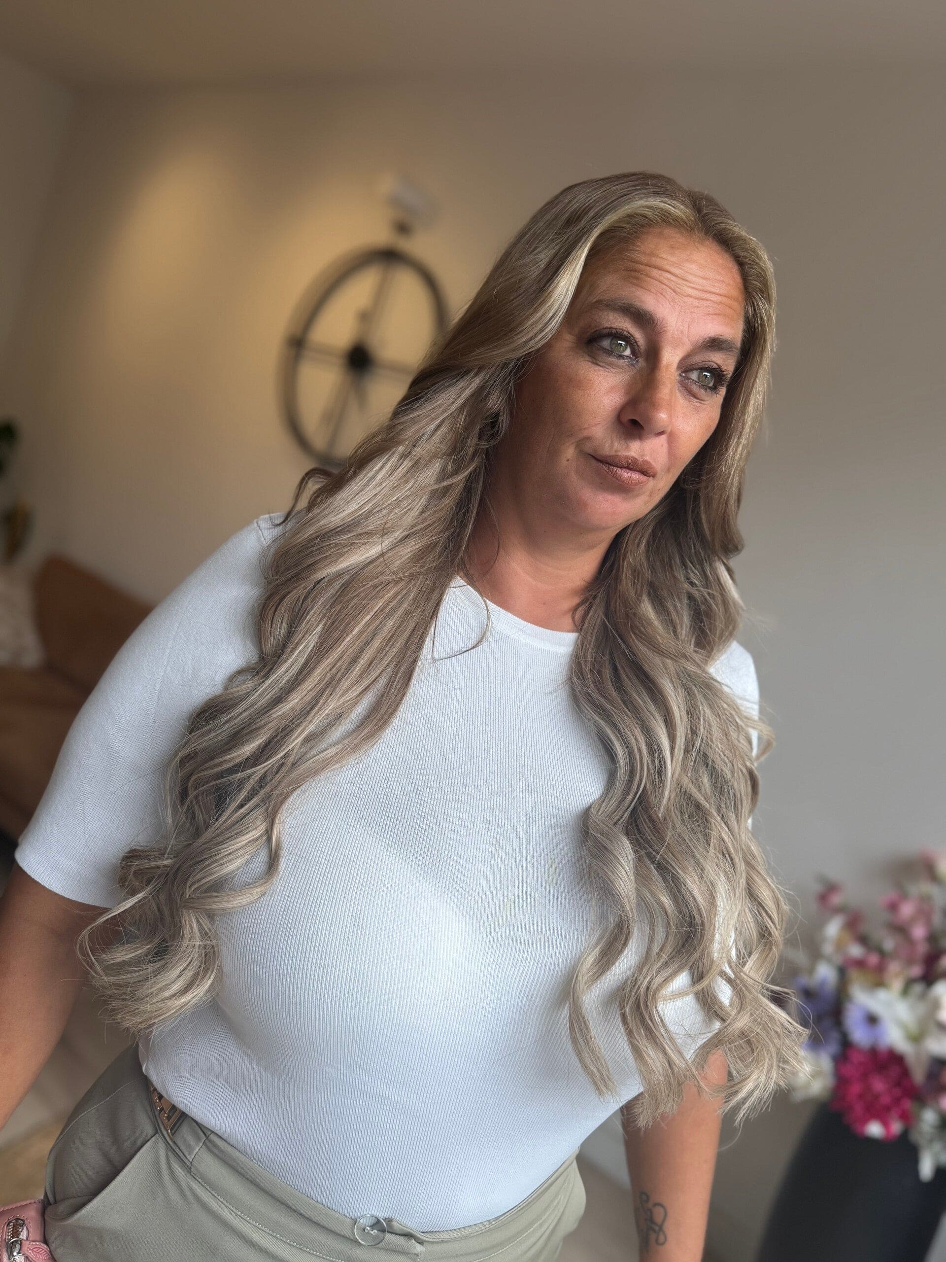 Lang, golvend blond haar met extensions, over de schouder gedragen.