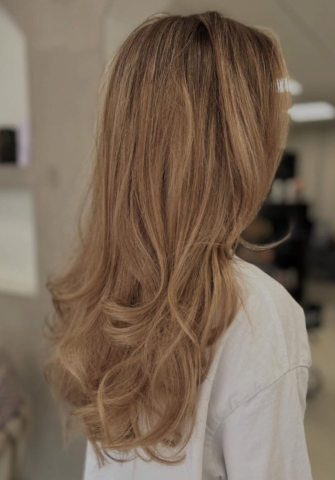 Lang karamelblond haar met een gelaagde coupe, van achteren gezien.